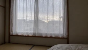 朝のカーテン越しの光が入る、片付いた寝室の窓辺