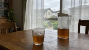 カーテン越しの窓と、卓上の麦茶のグラス